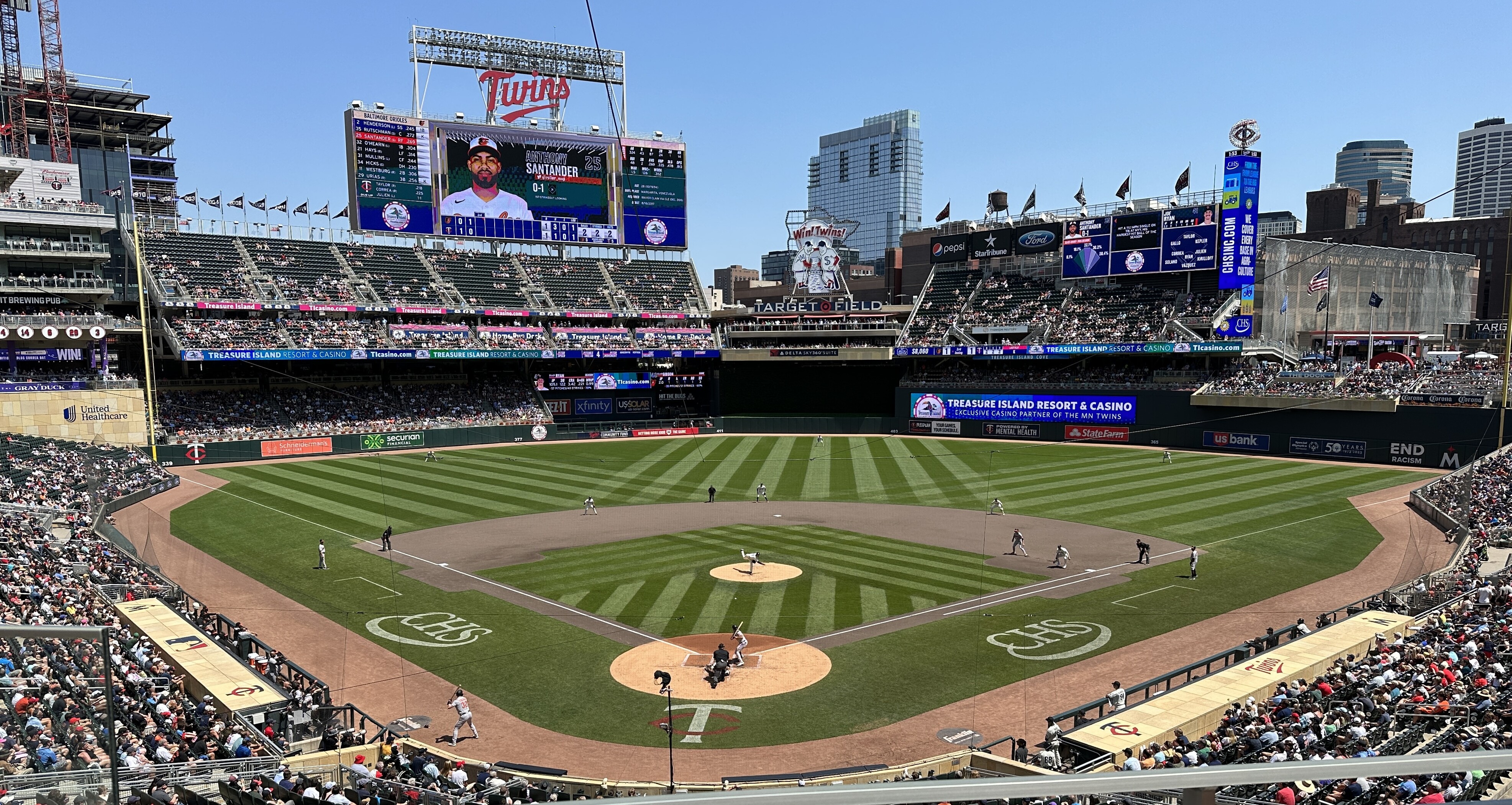 Sunny blue sky view of Target Field behind home plate with Joe Ryan throwing a pitch to Oriole hitter Anthony Santander