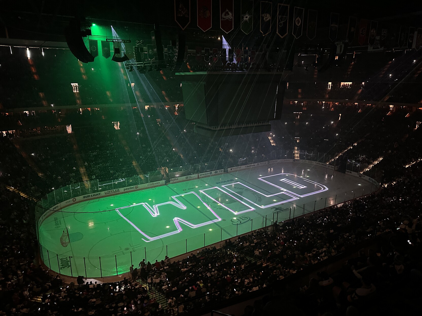 Hockey rink pre-game light show with green lasers spelling out WILD on the ice surface