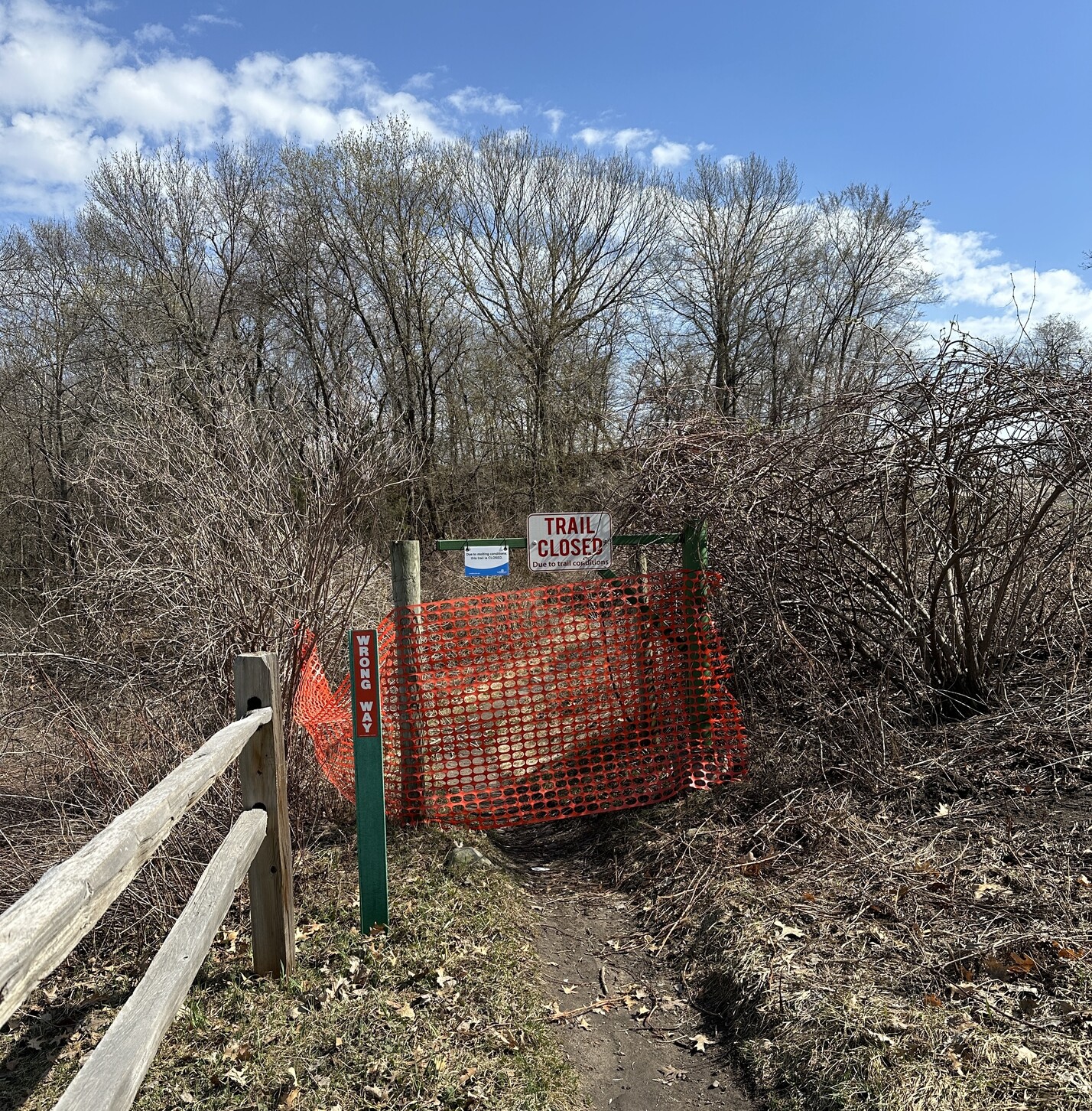 Blue sky, white clouds, orange fencing and a closed gate with signs telling bikers to stay off the trails for now @ Carver Lake Park in Woodbury, Minnesota