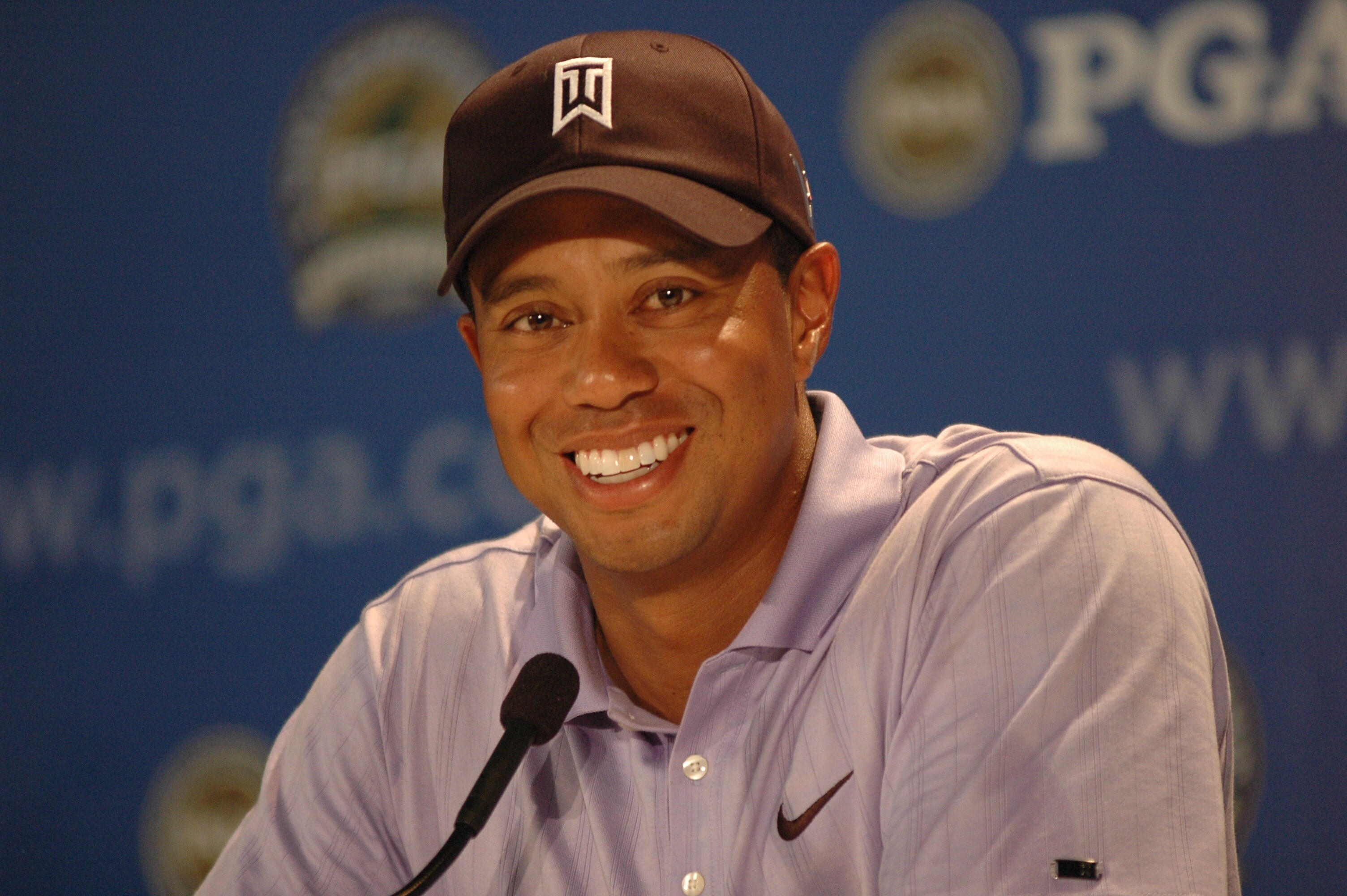 Close-up of Tiger Woods smiling in the interview room with a blue PGA backdrop