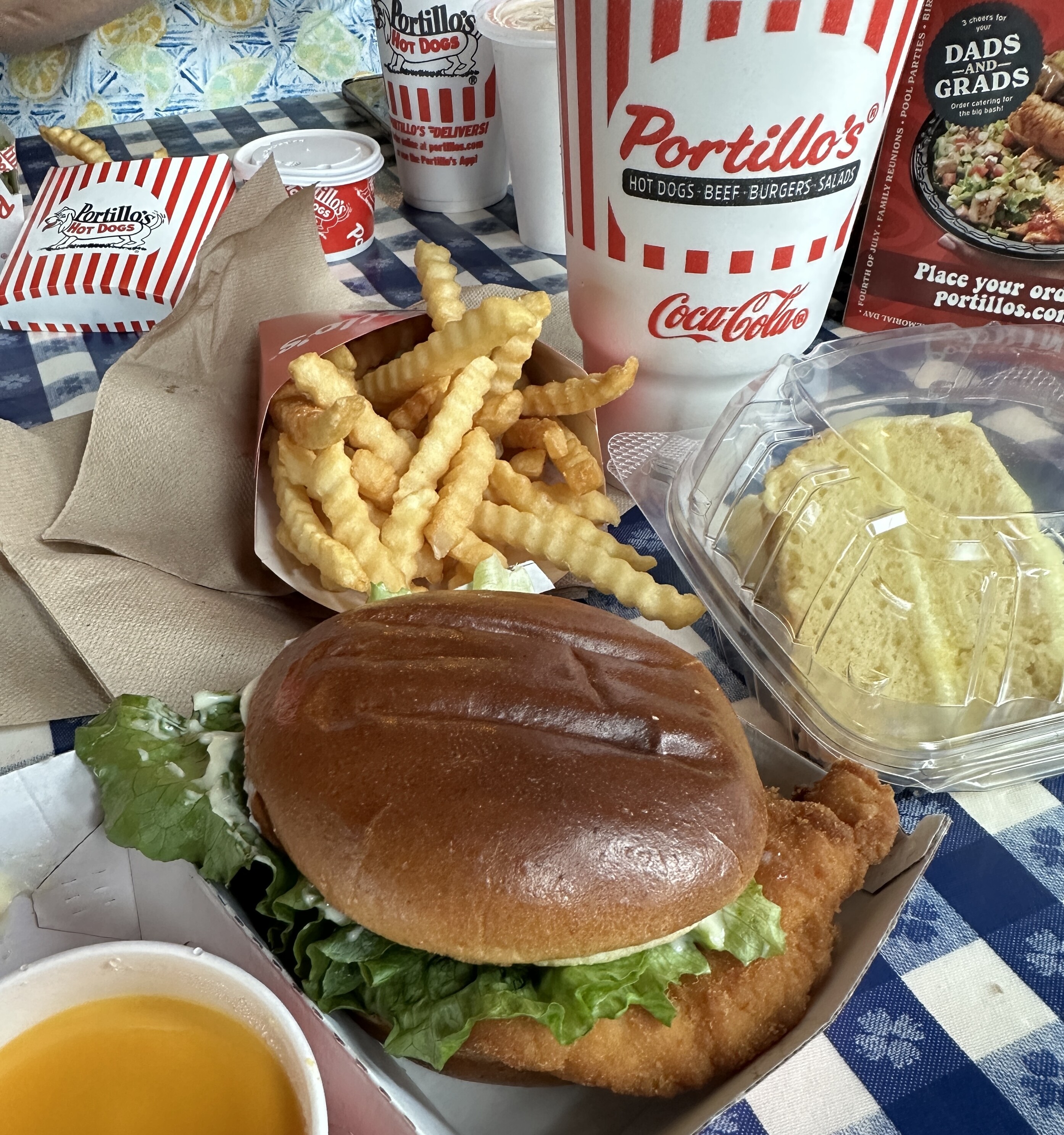 Chicken sandwich, cheese fries and lemon cake on a blue checkerboard table covering - Portillo’s Woodbury