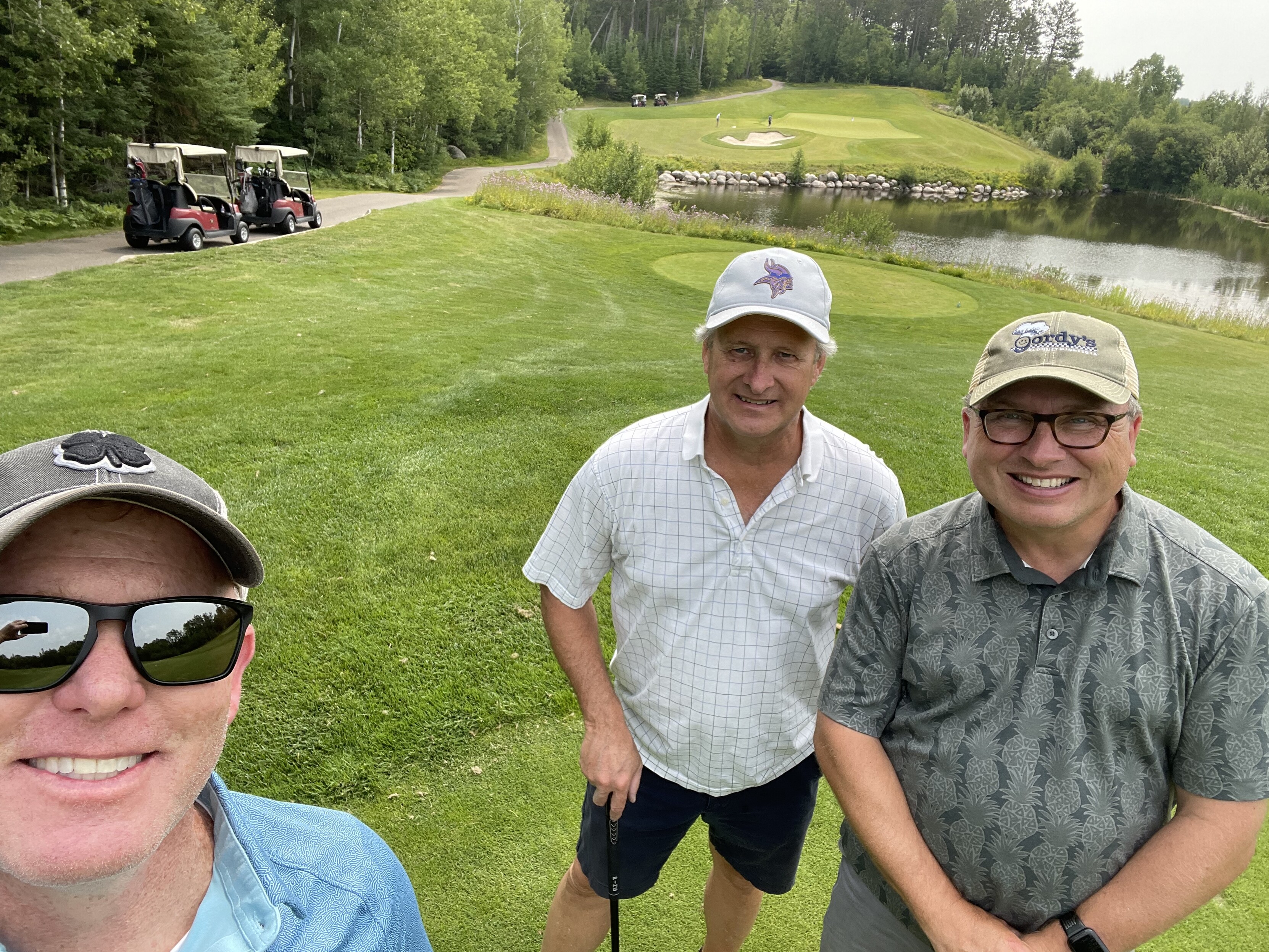 CS, LP and me on the third tee at The Wilderness at Fortune Bay golf course, with two golf carts in the background, a pond with boulders and the green off in the distance