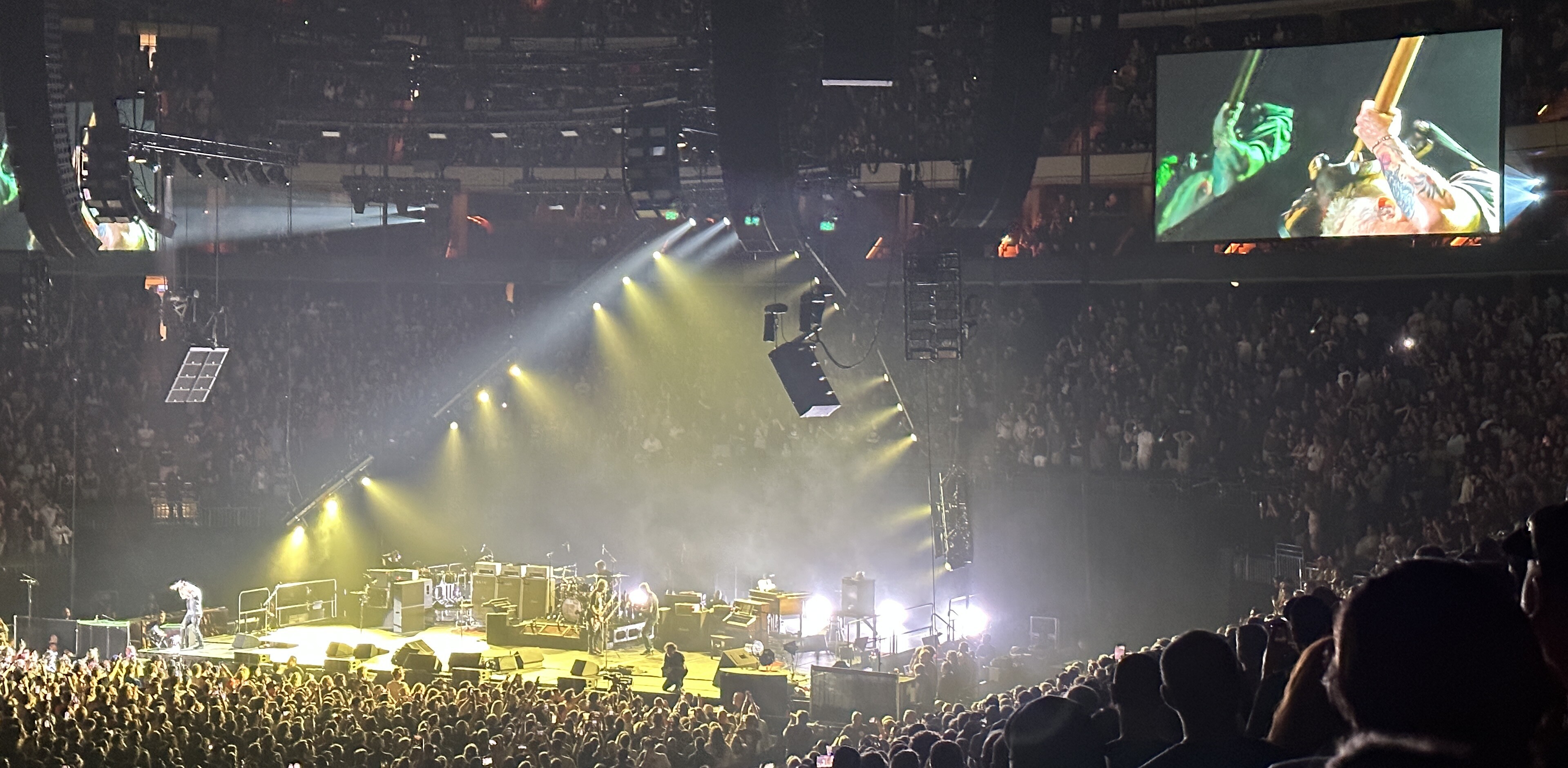 Very far away photo of the Pearl Jam concert at Xcel Energy Center in Saint Paul with the stage bathed in yellow spotlights with McCready far stage right and a video board hanging high stage left with a close-up of him holding his guitar behind his head