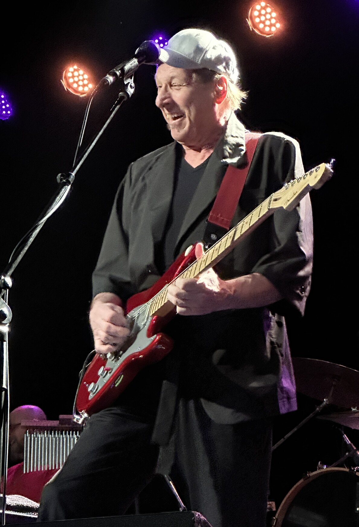 Adrian Belew on stage smiling and playing a red guitar