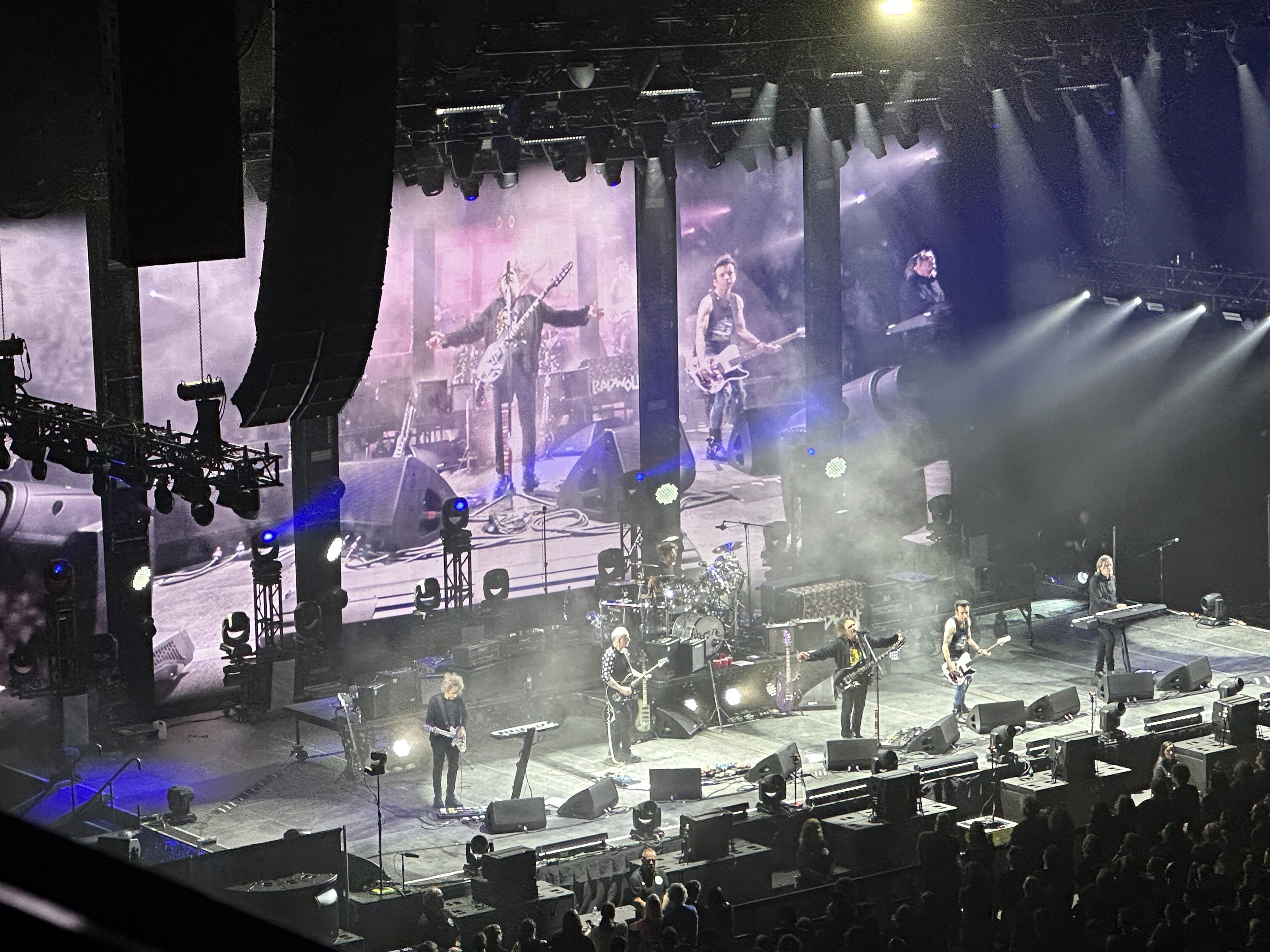 Shot of the stage from far away, with Robert Smith in the middle with arms outstreched and a giant video screen behind